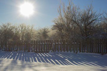 Winter snowy vintage old backyard wooden fence, beautiful shadows on sunny snow