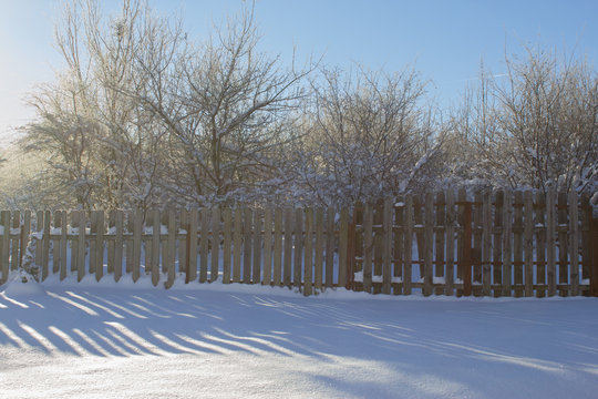 Winter snowy vintage old backyard wooden fence, beautiful shadows on sunny snow