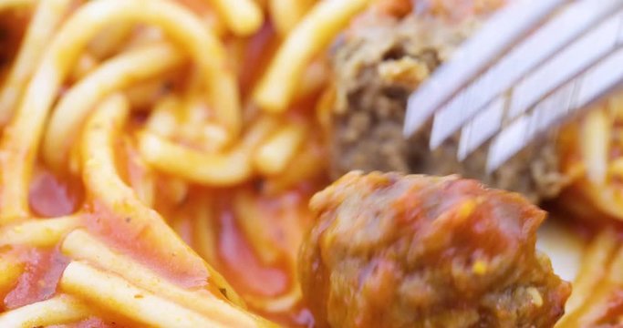 Close video of a spaghetti dinner on a plate with a fork cutting a meatball in half then eating the food.
