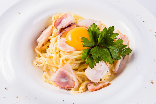 pasta with bacon and egg yolk on a white plate on a light background