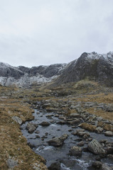 Portrait Glyderau llyn ideal river with boulders and snow capped mountains in the background in winter