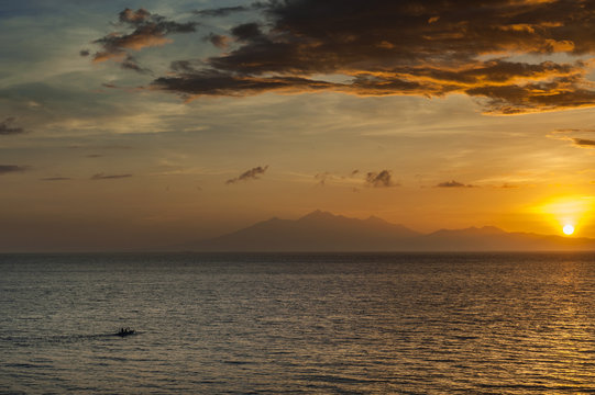 Sunrise Over Lombok Island, Indonesia. A dramatic sunrise over the Lombok Strait to the island of Lombok as seen from the Amed area of eastern Bali, Indonesia. Balinese fishing boats on the horizon.