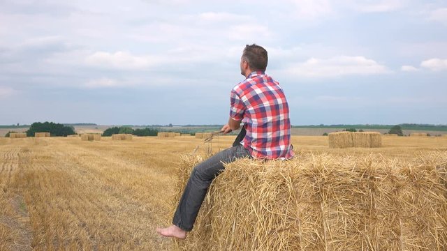 Young man sits on the hay in the field and looking on the horizon.