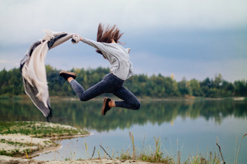 Extreme fit girl jump near lake with rug in hand