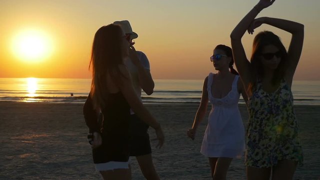 Young man dancing with three female friends on the shore of the ocean at twilight
