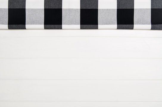 Top View Of Black Checkered Napkin Or Tablecloth On White Wooden Table With Visible Planks, Texture And Copy Space For Text.