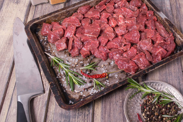 Raw meat with salt, pepper and rosemary on the baking pan on the wooden table