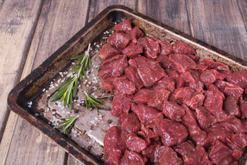 Raw meat with salt, pepper and rosemary on the baking pan on the wooden table