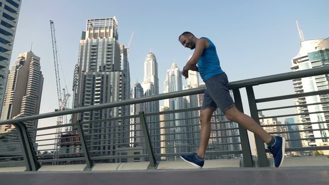 Young man using checking pulse while running on bridge in city, super slow motion 240fps
