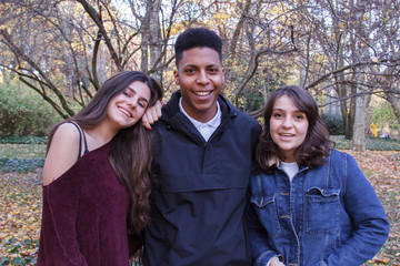 Two white Caucasian girls and one young black boy posing for a photo on a vacation trip. They are smiling in a park on an autumn day - friendship, multiracial, ethnic diversity, global concept 