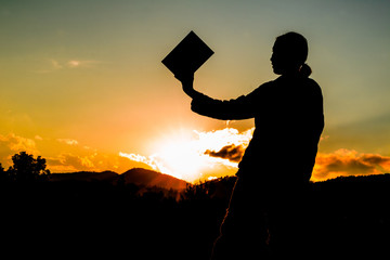 silhouette of a woman holding up a book