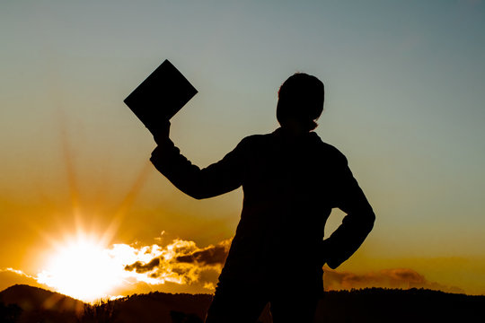 silhouette of a woman holding up a book