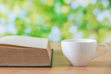 white coffee cup on wooden table with green leaves background