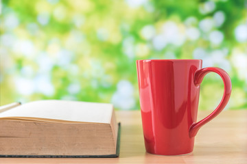red coffee cup on wooden table with green leaves background