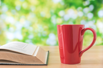 red coffee cup on wooden table with green leaves background