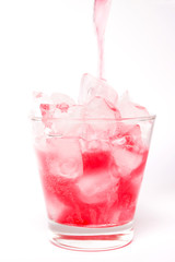 Pouring red sparkling wine in a glass with dancing bubbles on ice cubes isolated on white background