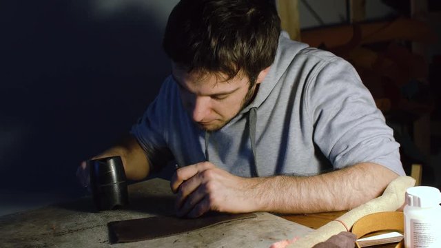 Man working on leather, making holes using hummer