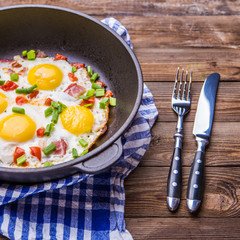 Fried eggs in pan with tomatoes and green fresh onion.