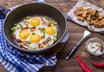 Fried eggs in pan with tomatoes and green fresh onion.