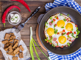 Fried eggs in pan with tomatoes and green fresh onion.