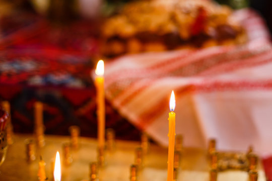 Single candle with dripping wax and blurring lights of many candles in two candlesticks at background.