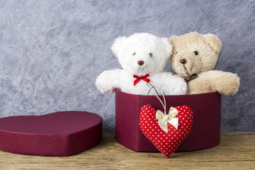 Love concepts of teddy bear in red heart gift box on wood table