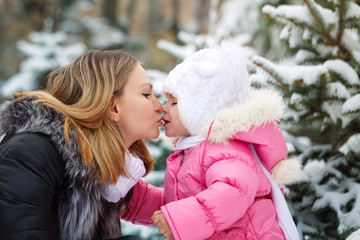 Mother kissing daughter in the nose outdoors. Family walk in a winter park. Family happiness.