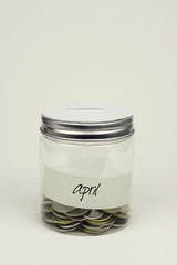 Saving coins money by monthly in a jar on a white background