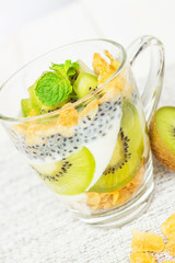 Delicious and healthy yogurt parfait made with homemade yogurt, kiwi fruit, corn flakes and sweet basil seeds on wooden background; healthy dietary start eating good food.