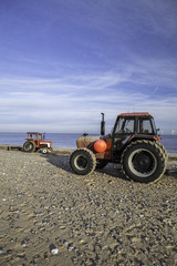 Pair of red tractors preparing for beach maintenance and the towing of boats.