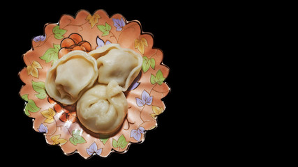 Three traditional pelmeni on a saucer decorated on a black background and right copy space