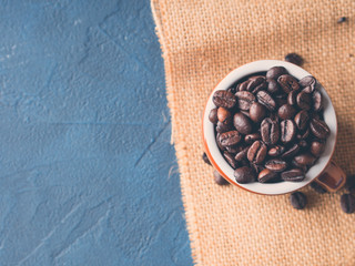 Coffee beans in italian espresso cup on burlap and dark blue black background