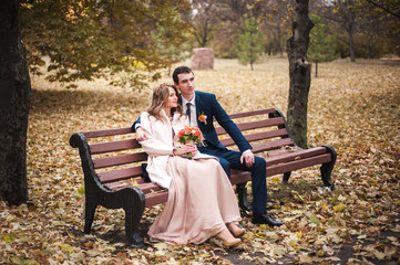 The beautiful bride and handsome groom sitting on a bench in the