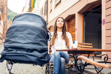 Young Mother With Baby Stroller Having Coffee At A Cafe