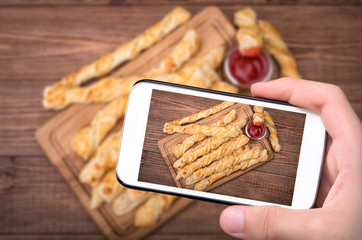Hands taking photo puff pastry cheese twists with smartphone.