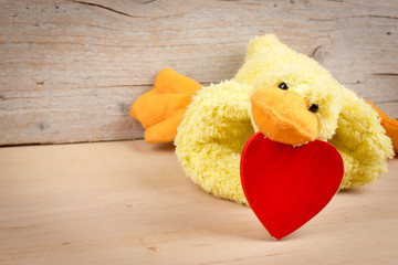 Sweet card for Valentine's Day with funny duck and red heart on wooden background. Empty space for text