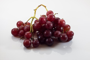 Isolated red grapes against a white background casting a reflection