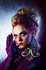 Young attractive blonde girl in bright art-makeup, high hair, body painting. Rhinestones and glitter