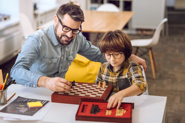 Happy son and father laying chess on the desk