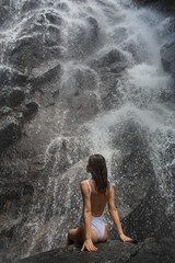 Beautiful slim model posing under waterfall wearing white swimwear 