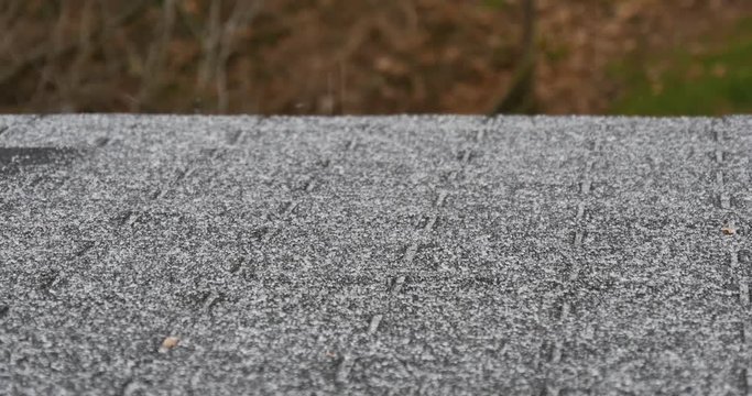 A panning shot of tiny, dangerous ice pellets falling on the rooftop of a residential home during a winter ice storm. With audio.  	