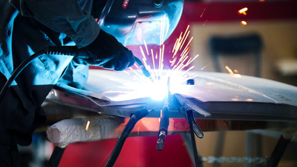 Welding industrial: worker in helmet repair detail in car service