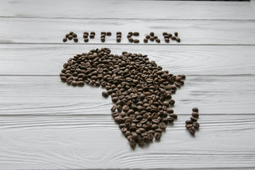 Map of the Africa made of roasted coffee beans laying on white wooden textured background and space for text