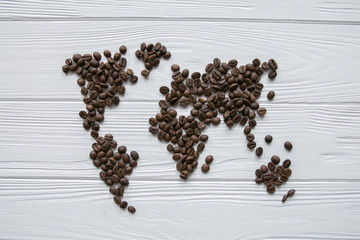 Map of the world made of roasted coffee beans laying on white wooden textured background with...