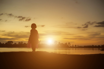 Silhouettes of mother and little daughter walking at sunset