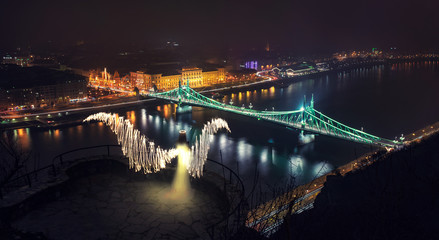 Fototapeta na wymiar Real angel over the river and the city bridge Budapest night