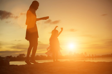 Silhouettes of mother and little daughter walking at sunset