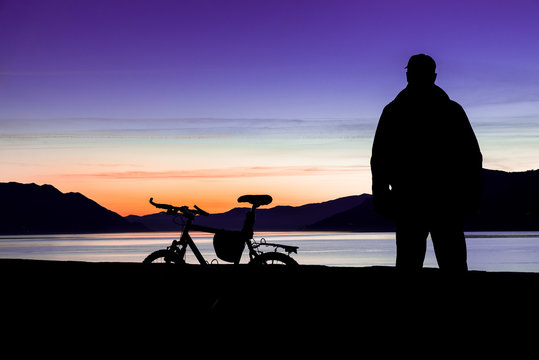Silhouette of a mountain bike and of a cyclist who is watching the sunset over the lake (lake Maggiore - Maccagno, Italy) - Focus on bike