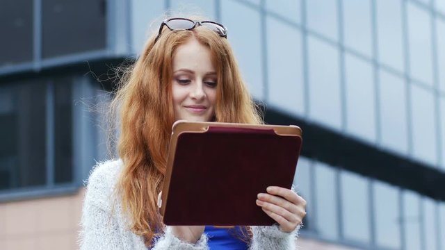 Beautiful, red-haired woman using a tablet in the city
