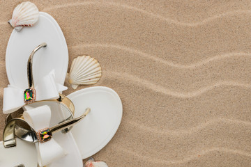 White flip-flops with rhinestones and seashell on the wavy sand.